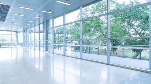 Blurred abstract background interior view looking out toward to empty office lobby and entrance doors and glass curtain wall with frame - blue white balance processing style